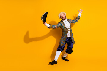 Young man dressed as a flamboyant nobleman in vintage attire dancing on a vibrant yellow...