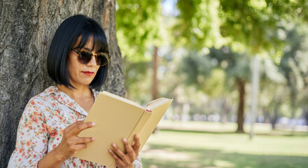 Hispanic woman in sunglasses reading a book in a sunny park setting