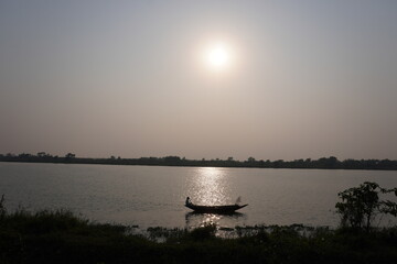 Naklejka premium A person is sailing a boat on the water near the river bank, sunset in the background