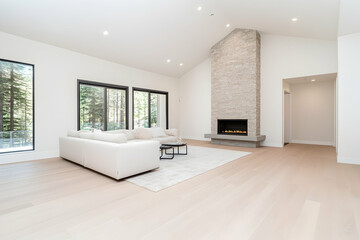 Modern open-concept living room with a stone fireplace and large windows overlooking a forest