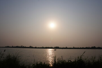 A beautiful sunset over a body of water, a lush foliage in the bank of the river