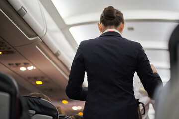 Rear view of a flight attendant in a black uniform on a plane with passengers. Hot drinks are served on board the aircraft. High quality photo
