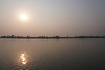 Fototapeta premium A serene moment of either a sunset over a river, with the sun's reflection visible on the surface
