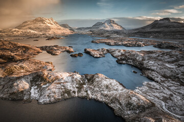 Stunning aerial view over the Loch Sionascaig lake with the snow capped peaks of Cul Mor, Cul Baeg and Stac Pollaidh on sunny winter day shortly before sunset and upcoming snow storm, Assynt, Scotland © Ji