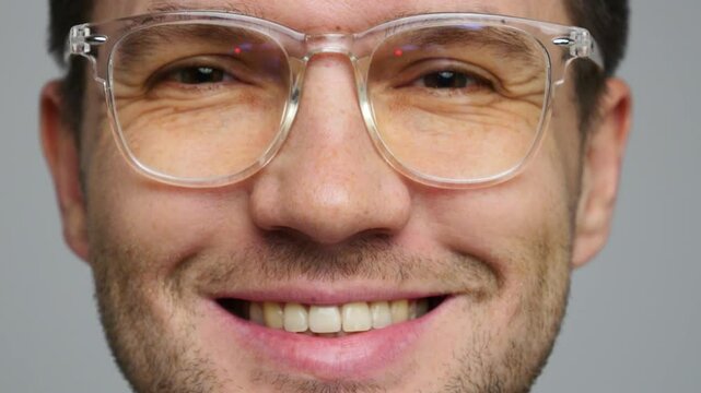 Close-up of a man with glasses smile, displaying a friendly expression against a neutral background
