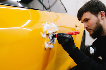 Car handle washing with microfiber and detergent in detailing auto service. Cleaner worker is...