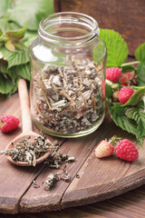 Dry raspberry leaf tea in glass jar with leaves and berry on rustic background, natural green medicine for menopause, pms, pregnancy, woman drink concept