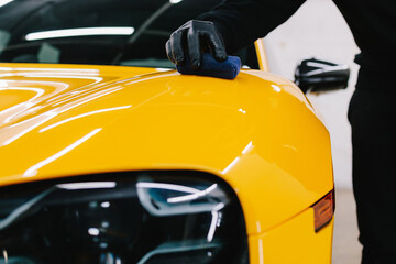 Detailing service worker applies ceramic protective liquid on the sports car. Smearing ceramic liquid to make protective nano layer for yellow sports car.
