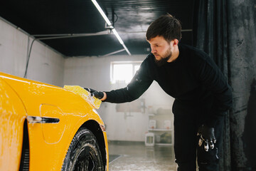 Procedure of washing car with soap solution and detergent before auto detailing. Worker cleans...