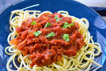 Spaghetti Bolognese with minced beef, onion, chopped tomato, garlic, olive oil, stock cube, tomato puree and Italian herb. Traditional Italian food with a fork on a plate.