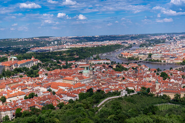 Obraz premium Panoramic view of Prague with the Vltava River, historic bridges, and red rooftops, surrounded by lush greenery. Stunning European cityscape showcasing Czech Republic’s architectural and natural beaut