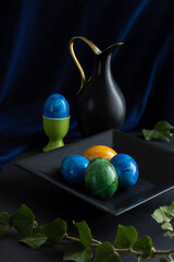 The photo depicts a still life arrangement featuring decorated eggs and a decorative pitcher