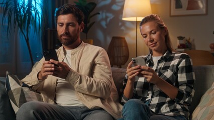 Gadgets addicted couple Caucasian man woman family using smartphones on couch evening night home internet social media overuse addiction girl guy husband wife browsing mobile phones online shopping