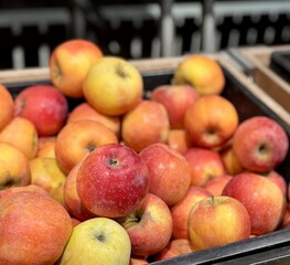 A mound of large red yellow coloured apples in boxes is displayed in the window of the supermarket's vegetable stand, demonstrating organic, vegetarian and healthy food. Close-up