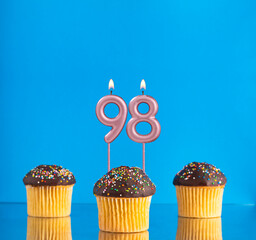 Three birthday cupcakes with number 98 candle - Blue background.