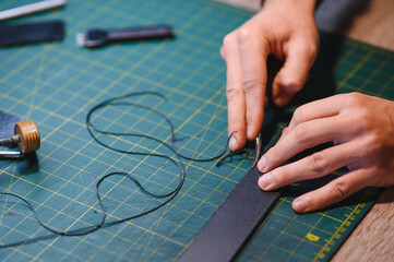 Asian male artisan carefully punching piece of leather at professional leather workshop