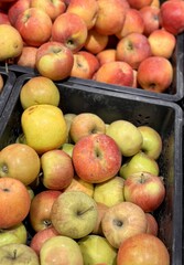 A mound of large red yellow coloured apples in boxes is displayed in the window of the supermarket's vegetable stand, demonstrating organic, vegetarian and healthy food. Close-up