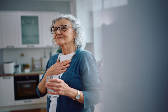 Pensive senior woman with glass of water in the kitchen.