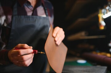 Production process. Young focused experienced master craftsman makes leather goods at his workplace