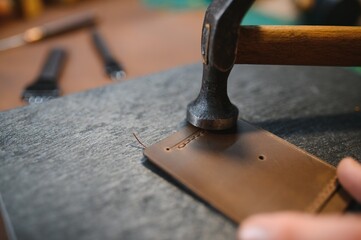 Production process. Young focused experienced master craftsman makes leather goods at his workplace