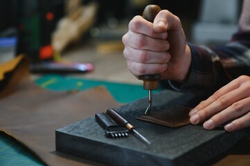 Production process. Young focused experienced master craftsman makes leather goods at his workplace
