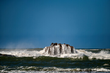 Waves crash against a rocky formation in Essaouira, Morocco during midday sun