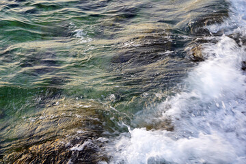 White wave and sea foam on top of rocks under turquoise sea water