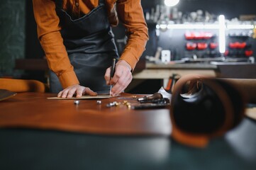 Production process. Young focused experienced master craftsman makes leather goods at his workplace