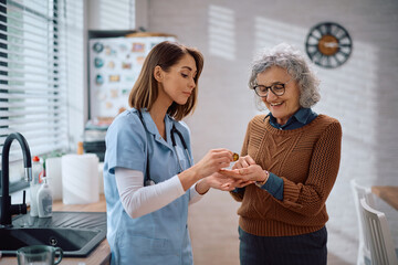 Obraz premium Visiting nurse giving pills to senior woman at home.
