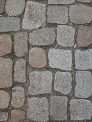 Old cobblestone pavement with a mix of gray and brown stones, creating a rustic and historic atmosphere. The worn texture and irregular shapes add character, making it perfect for backgrounds, archite