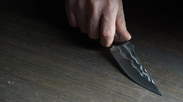 Man's hand takes a forged sharp knife from the wooden table, close up. Iron knife with shiny blade  in male hands