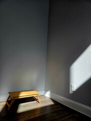 Sunlight gently streams through the window, casting a warm glow on the wooden table, while the rest of the room lingers in quiet darkness —  capturing a sense of stillness and solitude.