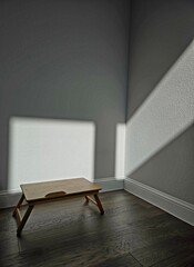 Sunlight gently streams through the window, casting a warm glow on the wooden table, while the rest of the room lingers in quiet darkness — capturing a sense of stillness and solitude.