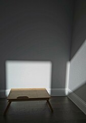 Sunlight gently streams through the window, casting a warm glow on the wooden table, while the rest of the room lingers in quiet darkness — capturing a sense of stillness and solitude. 