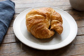 Croissant on White Plate with Dark Blue Linen Napkin on Rustic Wooden Table