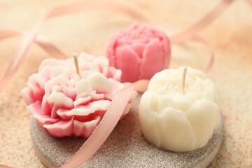 Beautiful flower-shaped candles and ribbon on beige background, closeup