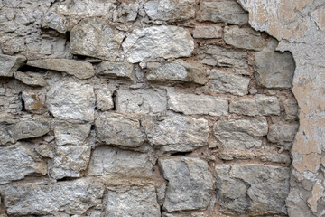 A wall made of limestone stones. The stones have crumbled in the wall of the building due to time and weather. The wall was built from the stones in ancient times.