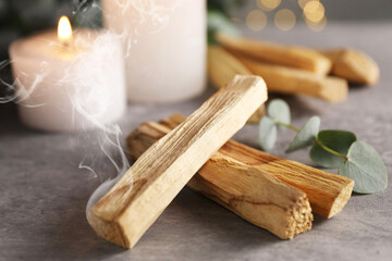 Palo Santo stick smoldering and burning candle on grey table, closeup