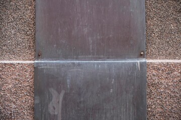 Rusty metal plates bolted onto rough stone surface, forming geometric industrial texture with weathered patina