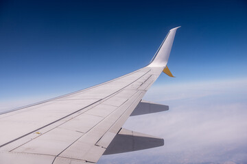 Obraz premium The wing of an airplane slices through the clear blue sky, offering a breathtaking view of the world from above, with a thin layer of clouds far below