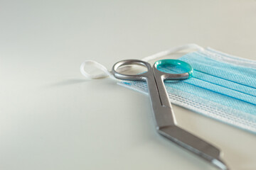 Curved scissors for surgery in medicine and disposable blue mask close-up. White background and free space for text.