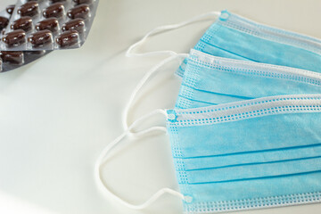 Blue disposable mask used in medicine. White background. Close-up photo. Vitamins/medicines in tablet form in the background.