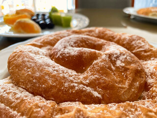 Ensaimada, traditional sweet pastry of the island of Mallorca, selective focus with a plate of fresh fruit in the background.