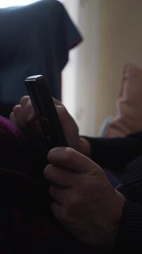 vertical detail video of man's hands browsing mobile phone on sofa