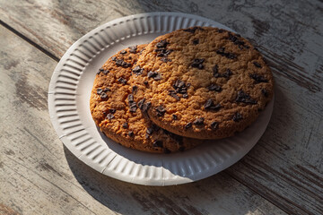 Early breakfast in the village – a large homemade cookie with chocolate chunks in warm sunlight on a simple wooden table.