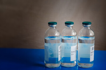 Saline solution for IV drip in a glass container on a blue medical table background – an...