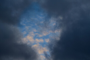 Dark rain clouds parted, revealing a view of white clouds in the blue sky. Symbolizes cleansing, release, hope, and renewal.