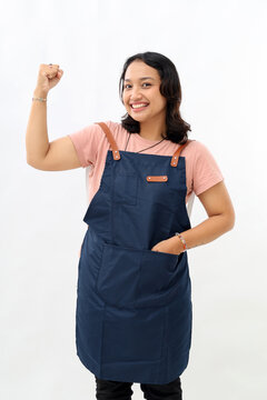 Cheerful asian seller making fist pump, rejoicing and triumphing, standing in blue apron against white background.