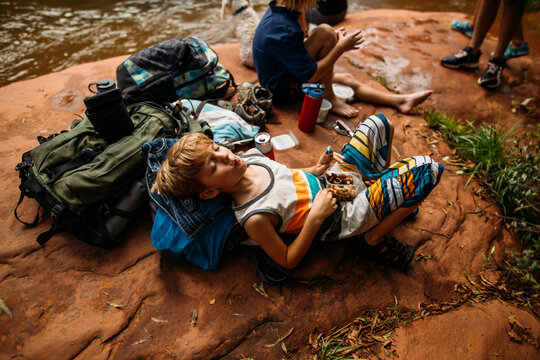 Boy laying on backpack in the woods having a snack