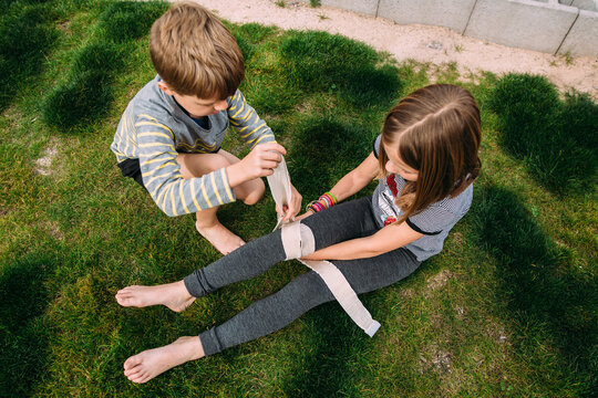 Boy helping girl bandage her leg in backyard